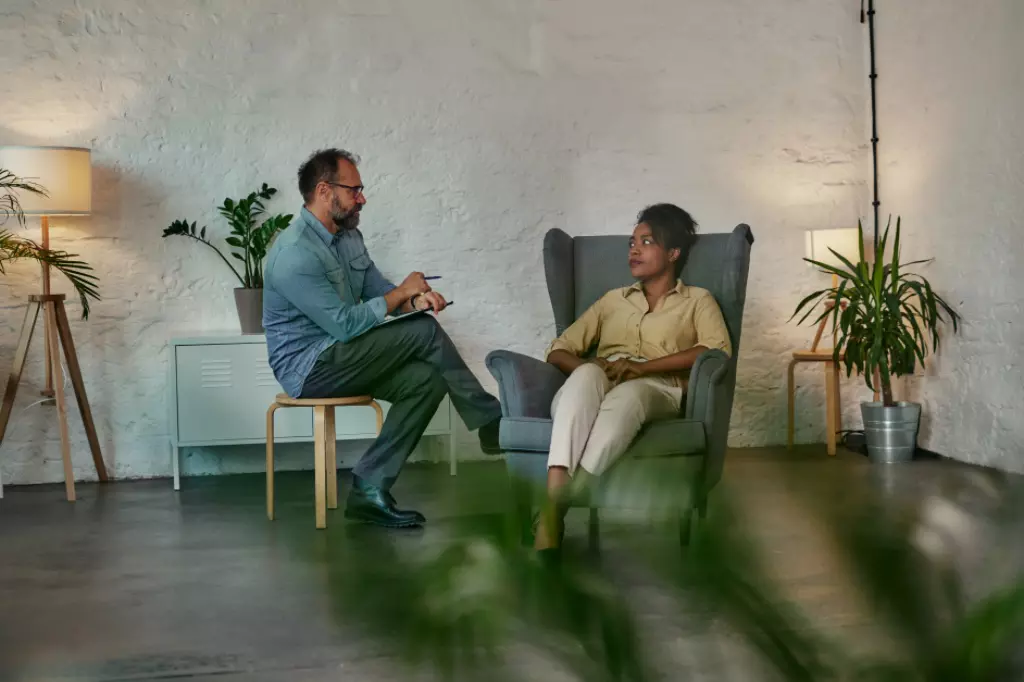 Dos personas en un ambiente de oficina relajado, una sentada en un sillón verde y la otra en un taburete, entablaron una conversación de apoyo.