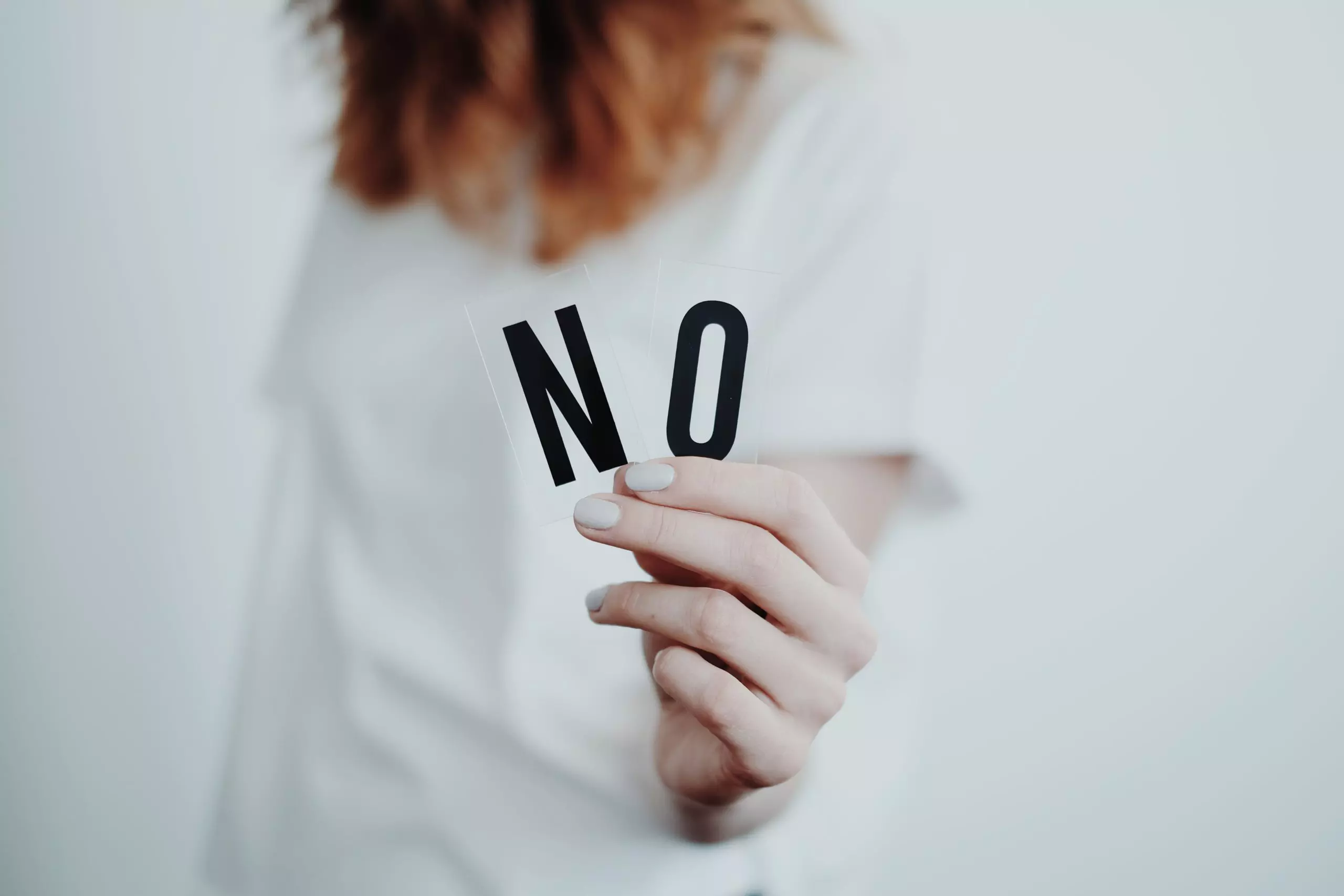 Persona con camisa blanca sosteniendo tarjetas con las letras "n" y "o" sobre un fondo blanco.