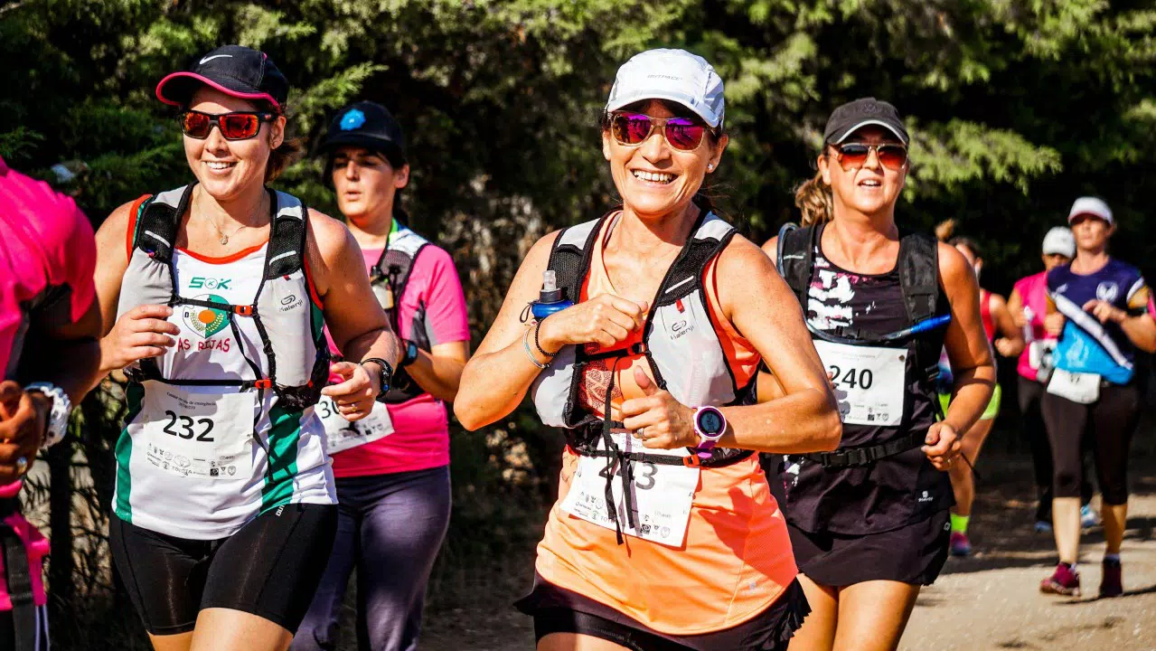 Un grupo de corredores, ataviados con indumentaria deportiva y dorsales, participan en una carrera al aire libre en un día soleado, irradiando bienestar y vitalidad.